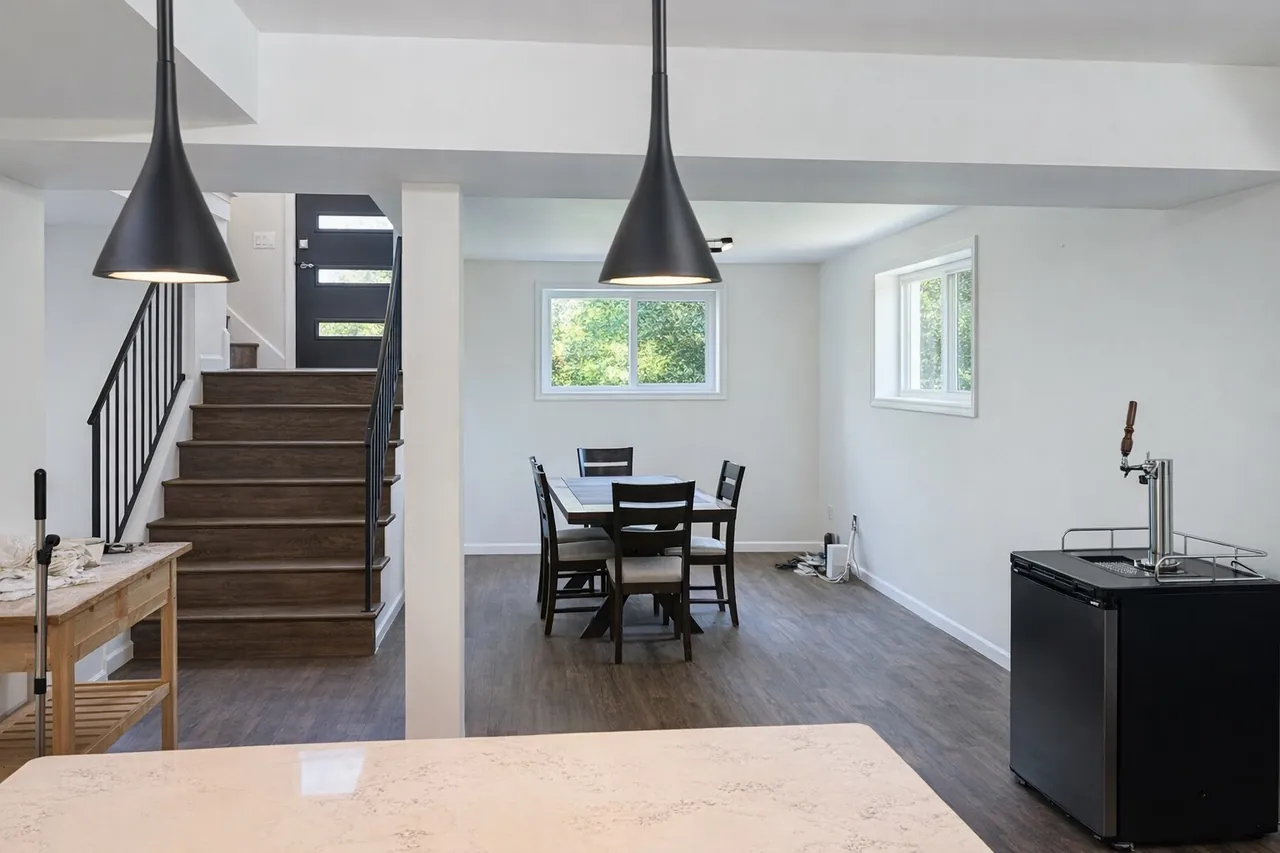 Bright open-plan basement dining area with sculptural black pendant lights and a staircase after real estate enhancement