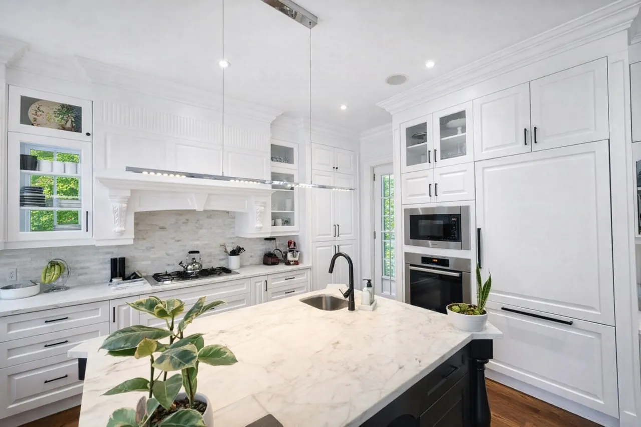Bright classic white kitchen with a marble island, shaker cabinets and stainless appliances after real estate photo enhancement