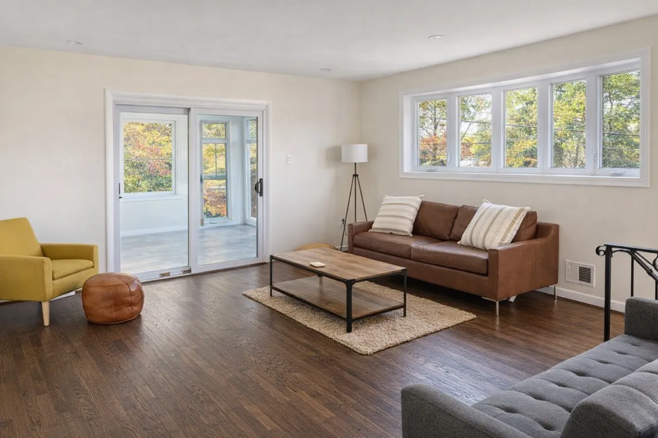 Bright mid-century living room with a cognac leather sofa, mustard accent chair and daylit windows after photo enhancement