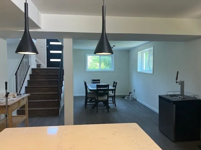 Bright open-plan basement dining area with sculptural black pendant lights and a staircase after real estate enhancement (original, before AI enhancement)