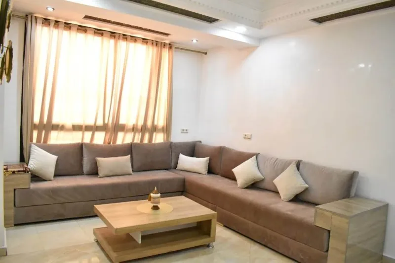 Bright traditional Moroccan-style living room with a taupe sectional, sheer curtains and ornate ceiling molding after photo enhancement (original, before AI enhancement)
