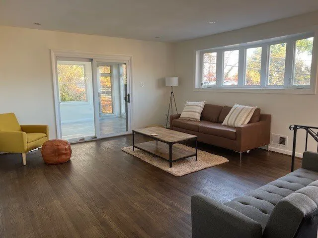 Bright mid-century living room with a cognac leather sofa, mustard accent chair and daylit windows after photo enhancement (original, before AI enhancement)